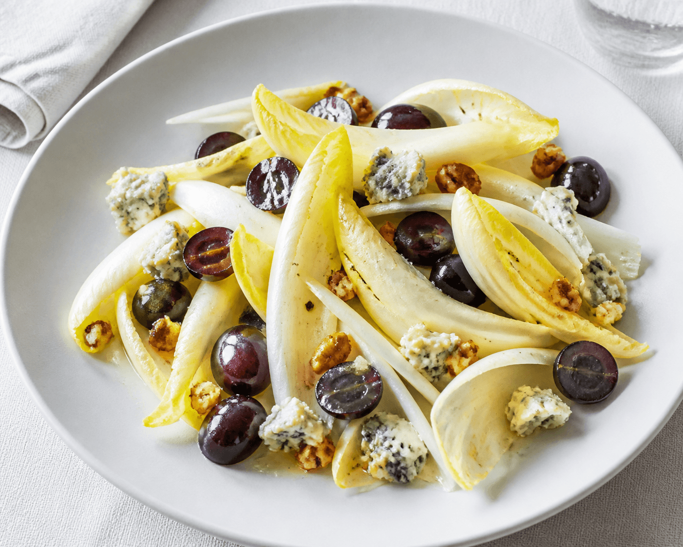 Salade d'endives avec raisin noir, roquefort et vinaigrette dans une assiette claire.